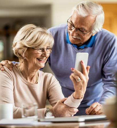 Happy senior woman using cell phone with her husband at home. Happy mature couple using smart phone at home.