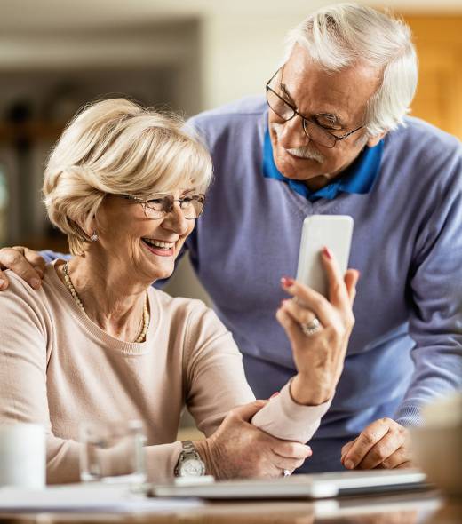 Happy senior woman using cell phone with her husband at home. Happy mature couple using smart phone at home.